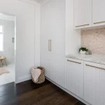 A photo of a laundry room, connected to a bathroom, a bath in the background.