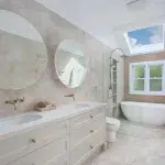 A photo of a bathroom, with a sink, 2 round mirrors, toilet, shower and bathtub.